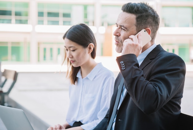 Business people on bench with laptop and smartphone