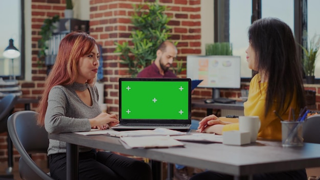 緑色の画面でラップトップを見て、パートナーシップの開発に取り組んでいるビジネスマン。クロマキーの背景とコンピューター上のコピースペースを持つ分離されたモックアップテンプレートを使用している同僚。 Premium写真
