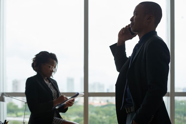 Business people talking on phone and writing in notebook against office window