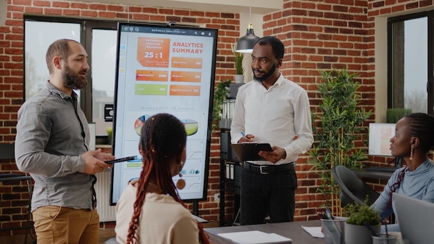 Business people using monitor to do financial presentation at conference with coworkers. Men sharing data analysis and marketing strategy with group of colleagues at briefing meeting.