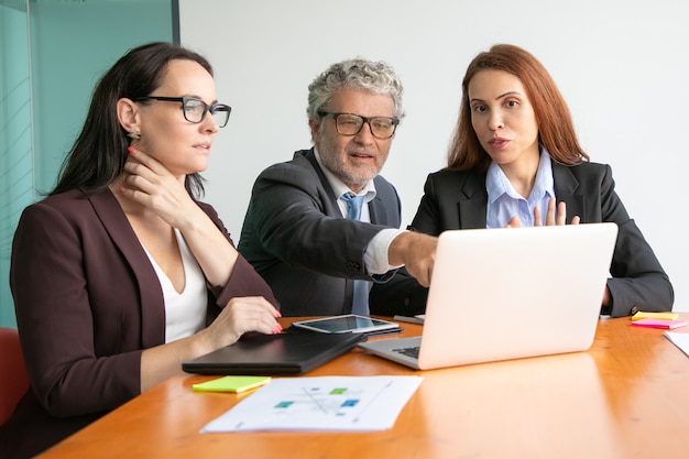 Business people watching and discussing presentation on laptop, looking and pointing at display