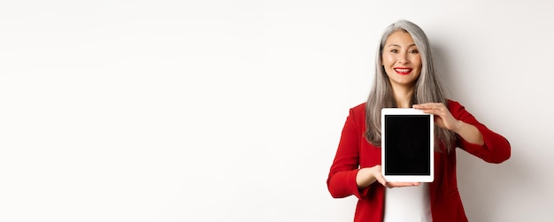 Free photo business proud asian female manager showing blank digital tablet screen smiling and demonstrating pr