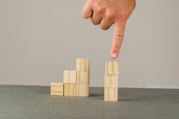 Business strategy concept on grey and white wall side view. man showing wooden blocks tower.