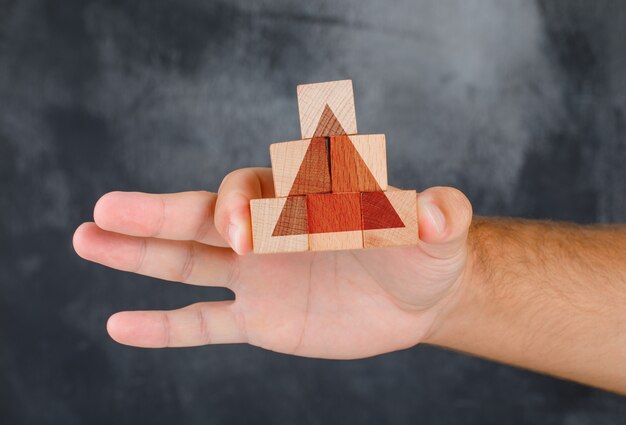 Business strategy concept side view. hand holding pyramid of wooden block.