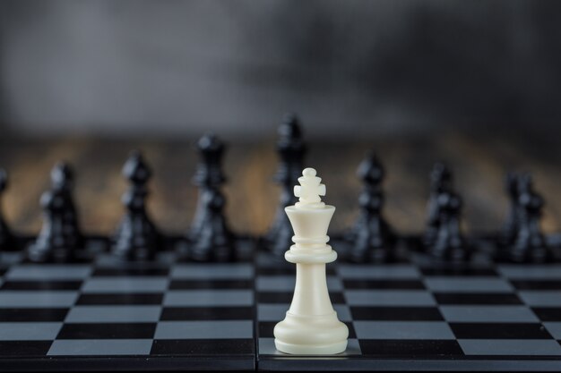 Business strategy concept with figures on chessboard on blurred and wooden table side view.