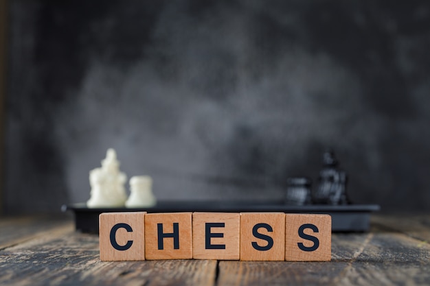 Business strategy concept with figures on chessboard, wooden cubes on foggy and wooden table side view.