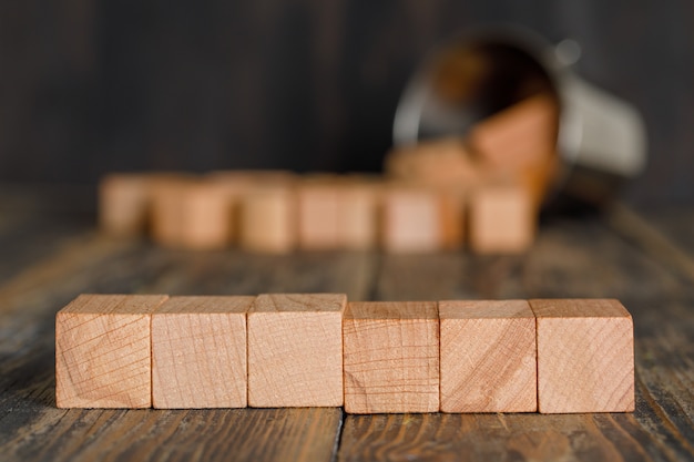 Business strategy concept with scattered wooden cubes from bucket on wooden table side view.