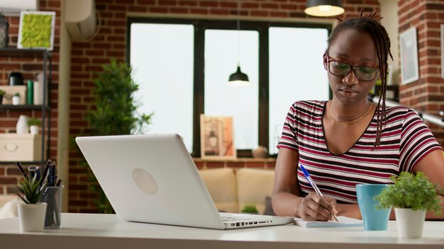 Business student taking notes at online webinar class on laptop, doing remote work and distant education lesson. Working remotely on startup and learning modern freelance job at home.