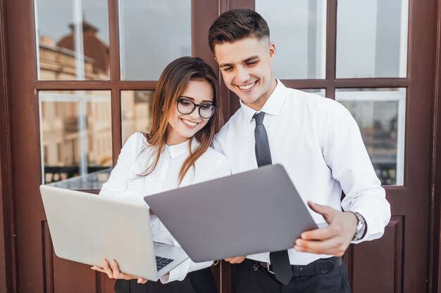 Business style. Young beautiful woman with glasses and a guy in a business image with a laptop in their hands smiling