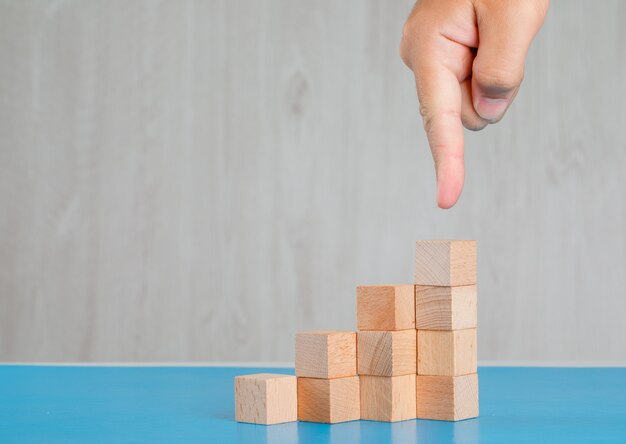 Business success concept on blue and grey table side view. finger showing stack of wooden cubes.