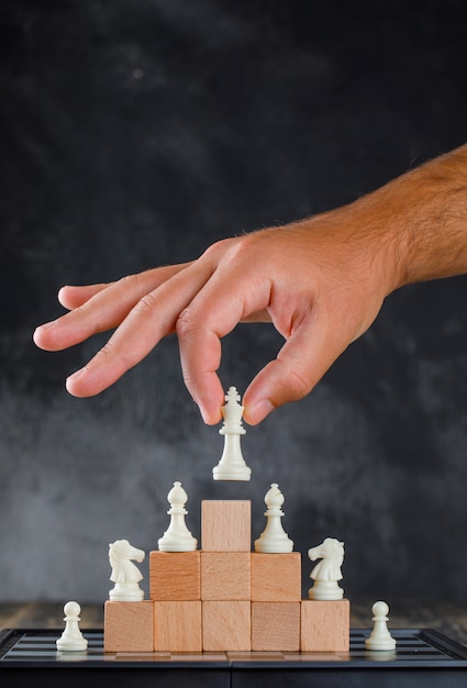 Business success concept with chessboard side view. man placing figure on pyramid of blocks.