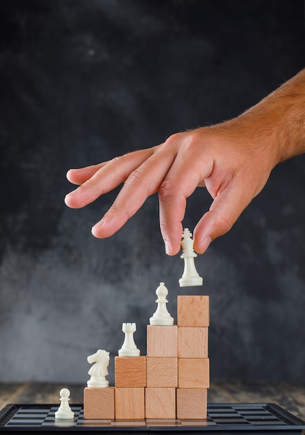 Business success concept with chessboard side view. man placing figure on pyramid of blocks.