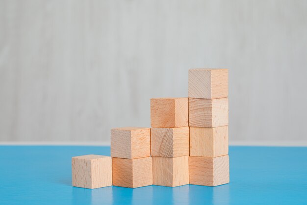 Business success concept with stack of wooden cubes on blue and grey table side view.