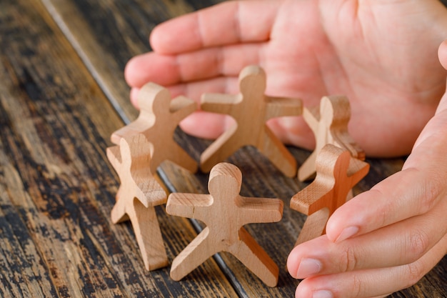 Business success concept on wooden table top view. hands protecting wooden figures of people.