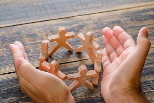 Business success concept on wooden table top view. hands protecting wooden figures of people.