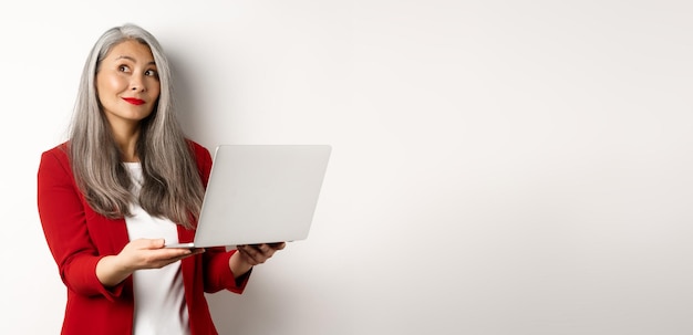 Foto gratuita business donna d'affari asiatica di successo in blazer rosso imaging qualcosa che lavora su laptop e lookin