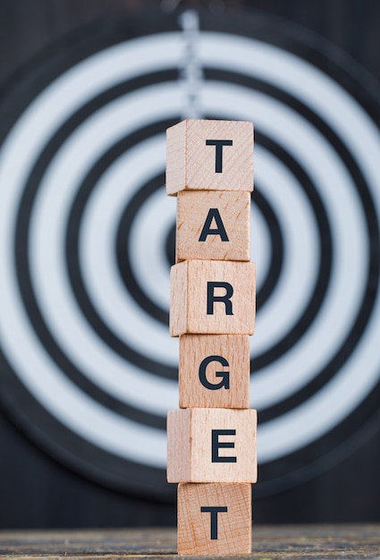 Business target concept with dartboard, wooden cubes on wooden and black background side view.