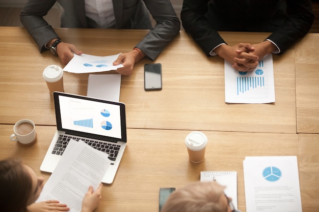 Business team brainstorming analyzing statistics report at meeting, top view