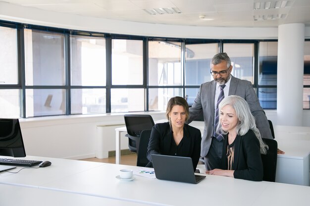 Business team of three watching presentation on pc monitor, discussing project, sitting at workplace and pointing at display. Copy space. Business meeting concept