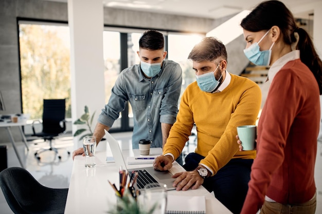 Business team with protective face masks working on laptop in the office