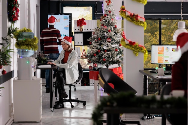 クリスマスの休暇の間に ⁇ 忙しい祭りの装飾されたオフィスで働くビジネスチーム ⁇ 勤勉な従業員がクリスマスの装飾されたワークスペースで様々な会社プロジェクトのタスクを解決しています ⁇ 