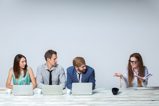 Business team working together at office on light gray background. all working on laptops. boss reading notebook. copyspace image