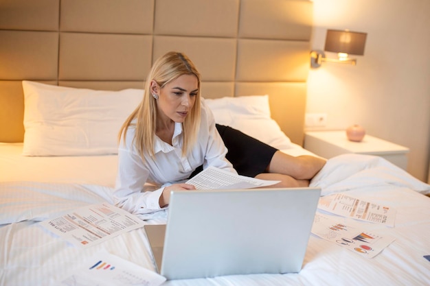 Бизнес-технологии Интернет и концепция отеля счастливая деловая женщина с ноутбуком, лежащая в отеле в постели и работающая допоздна в гостиничном номере со своим ноутбуком