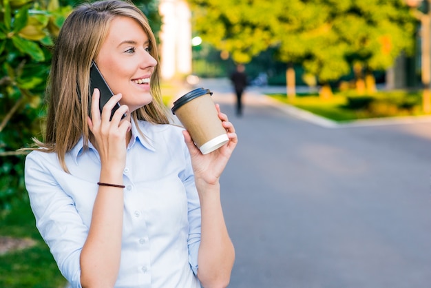 business, technology and people concept - smiling businesswoman with smartphone over office building