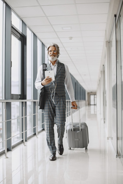Foto gratuita viaggio di lavoro. concetto aziendale e di persone. maschio in abito grigio. anziano con tablet e cuffie.