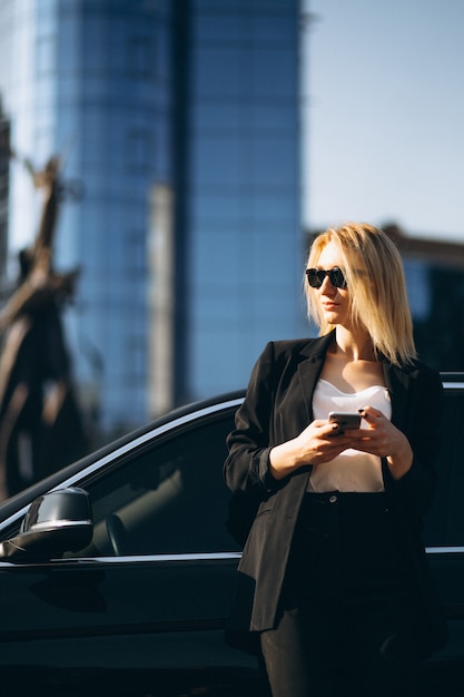 Free photo business woman by the car in town using phone