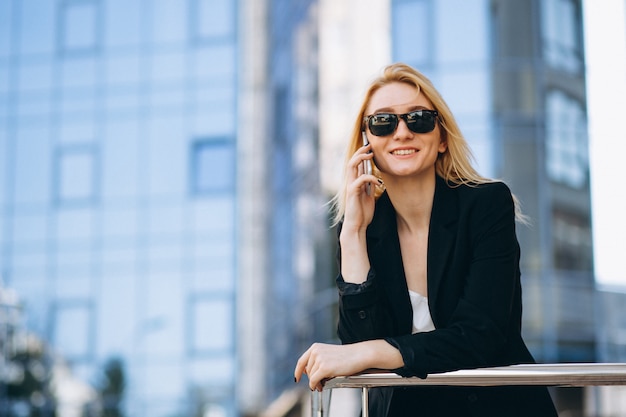 Business woman by the skyscraper using phone