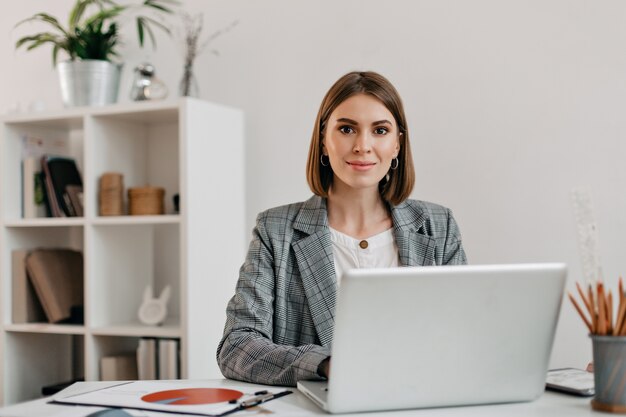 Business woman in checkered jacket with smile while sitting at desk in her office.