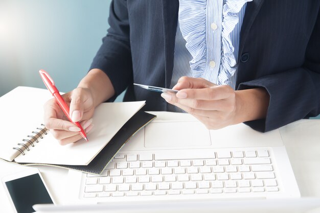 Деловая женщина в темный костюм, проведение кредитной карты, используя ноутбук и написание на ноутбуке, Бизнес и онлайн-покупки концепции