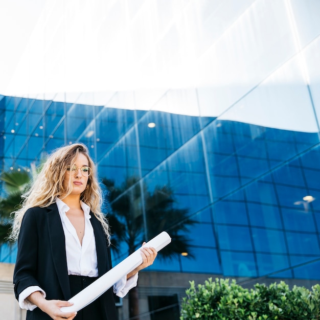 Business woman in front of glass building holding plan