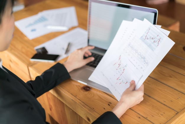 Foto gratuita mano donna di affari con grafici finanziari e computer portatile sul tavolo.