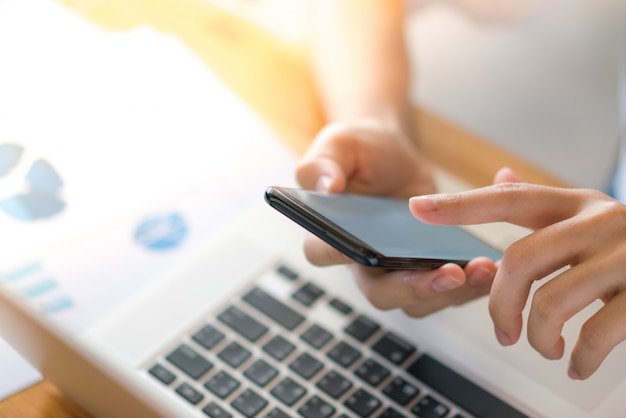 Business woman hand with Financial charts and mobile phone over laptop on the table .