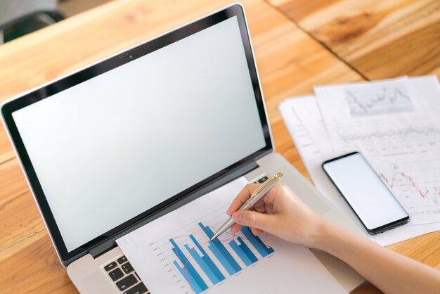 Business woman hand with Financial charts and mobile phone over laptop on the table .