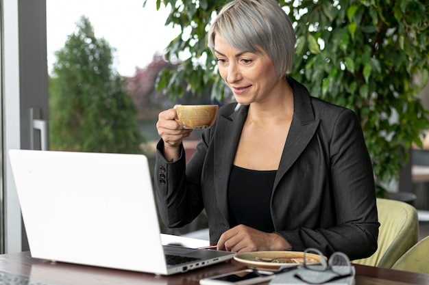 Foto gratuita donna di affari che mangia caffè mentre lavorando