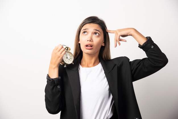 Business woman holding an alarm clock on white wall.