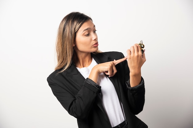 Business woman holding an alarm clock on white wall. 