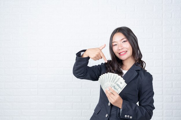 Бизнес женщина, держащая банкноты, наличные деньги отдельно, белая кирпичная стена Сделанные жесты с языком жестов.