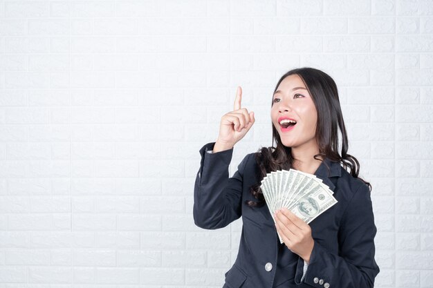 Business woman holding banknote, cash separately, white brick wall Made gestures with sign language.