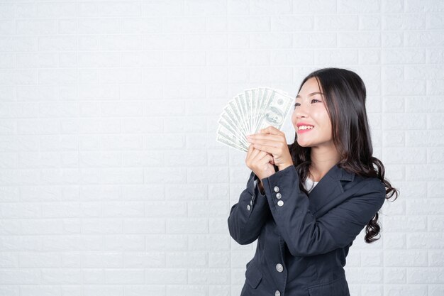 紙幣、現金を別々に保持している女性実業家、白いレンガの壁手話でジェスチャーをした。