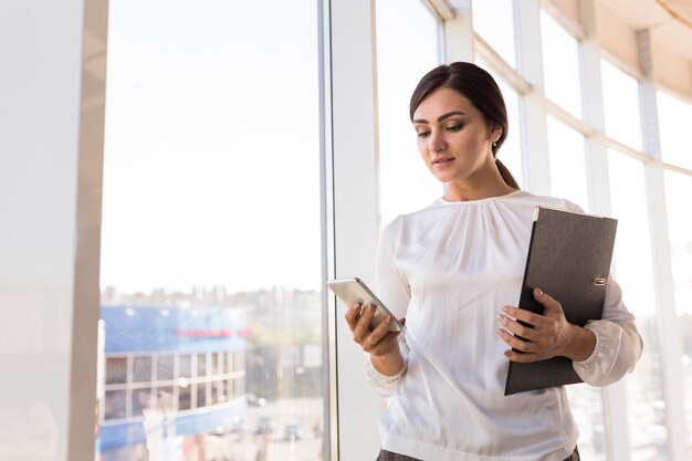 Business woman holding binder and looking at smartphone