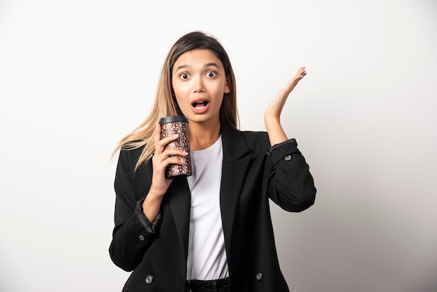 Business woman holding cup and posing on white wall . 