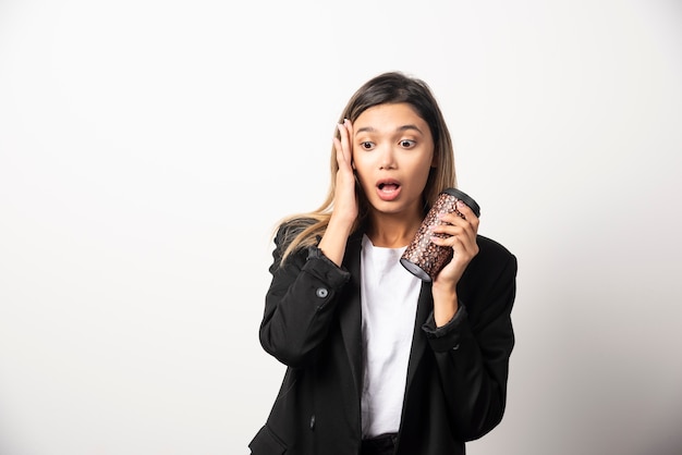 Business woman holding cup and posing on white wall . 