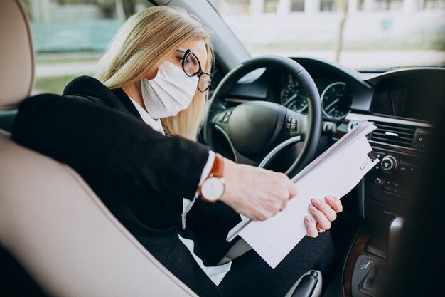 Business woman in protection mask sitting inside a car