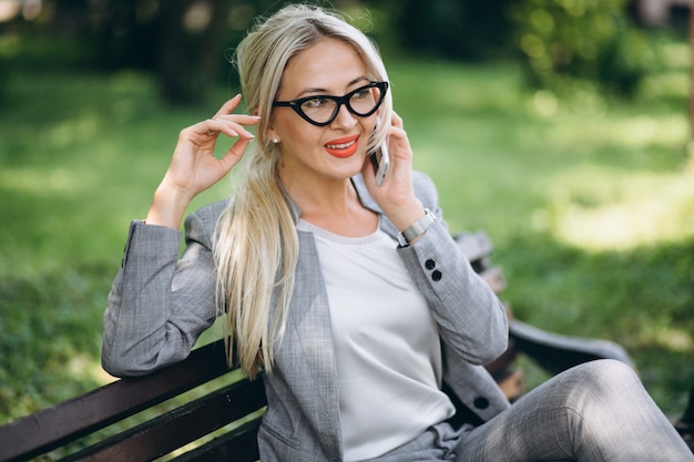 Donna di affari che si siede sul banco in sosta che comunica sul telefono