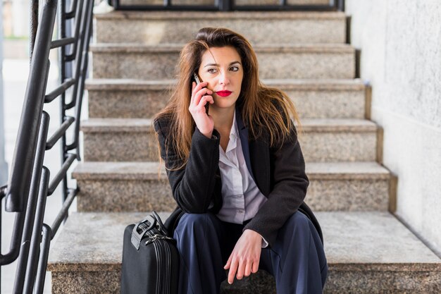 Business woman sitting on stairs and talking by phone 