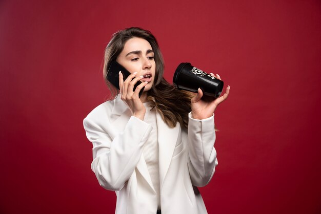 Business woman speaking on phone and looking on a coffee cup 